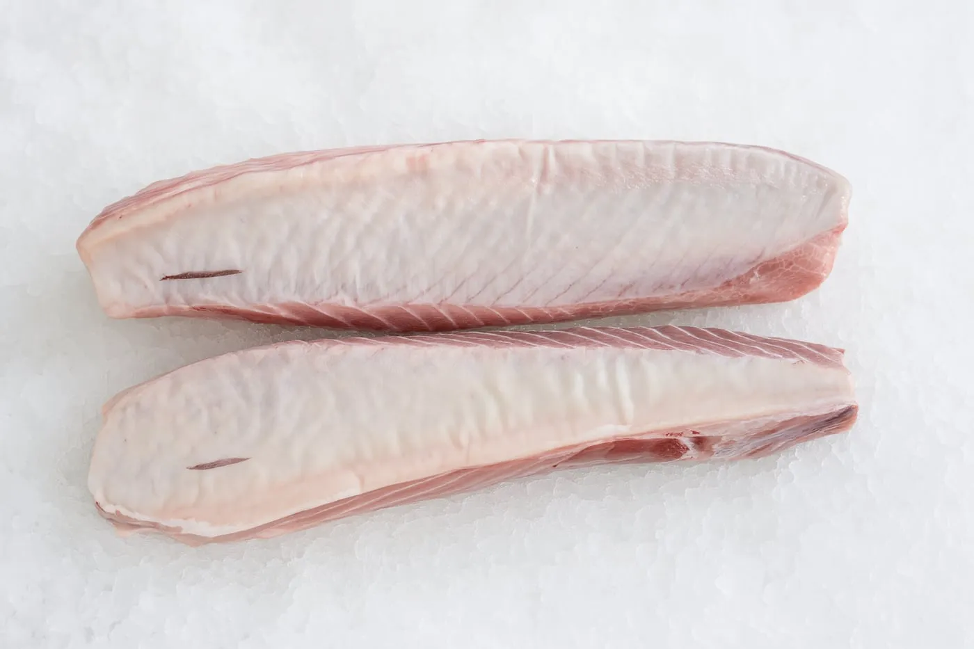 Two pale pink strips of yellowfin tuna belly on crushed ice